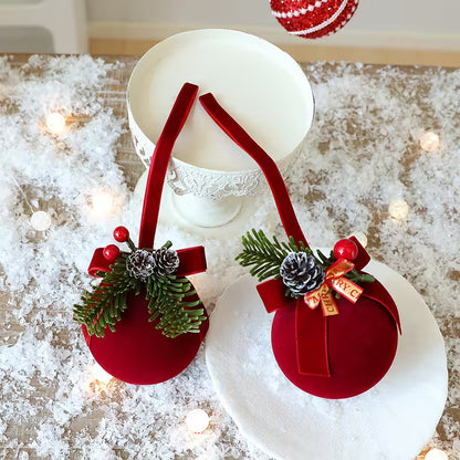 Red Christmas ornaments with greenery and ribbons on a snowy surface with lights.