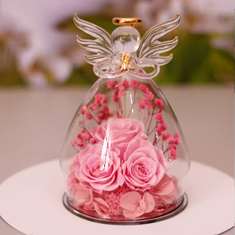 Glass dome with pink roses and an angel figurine on a blurred background