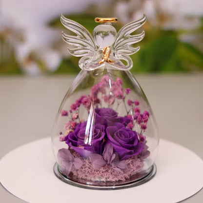 Glass dome with an angel figurine containing purple flowers on a white surface.