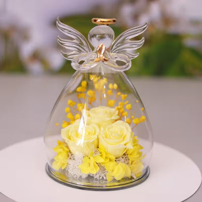 Decorative angel figurine with yellow flowers inside a glass dome on a white surface.