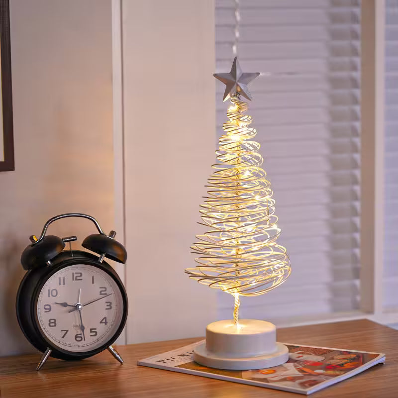 Decorative LED Christmas tree with a star on top next to a black alarm clock on a table.