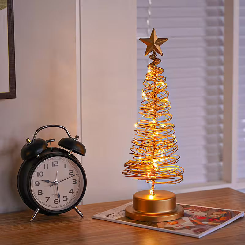 Decorative LED Christmas tree with star on top next to a black alarm clock on a table.