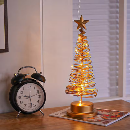 Decorative LED Christmas tree with star on top next to a black alarm clock on a table.