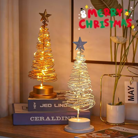 Two small Christmas trees with lights on a table, with a 'Merry Christmas' sign in the background.