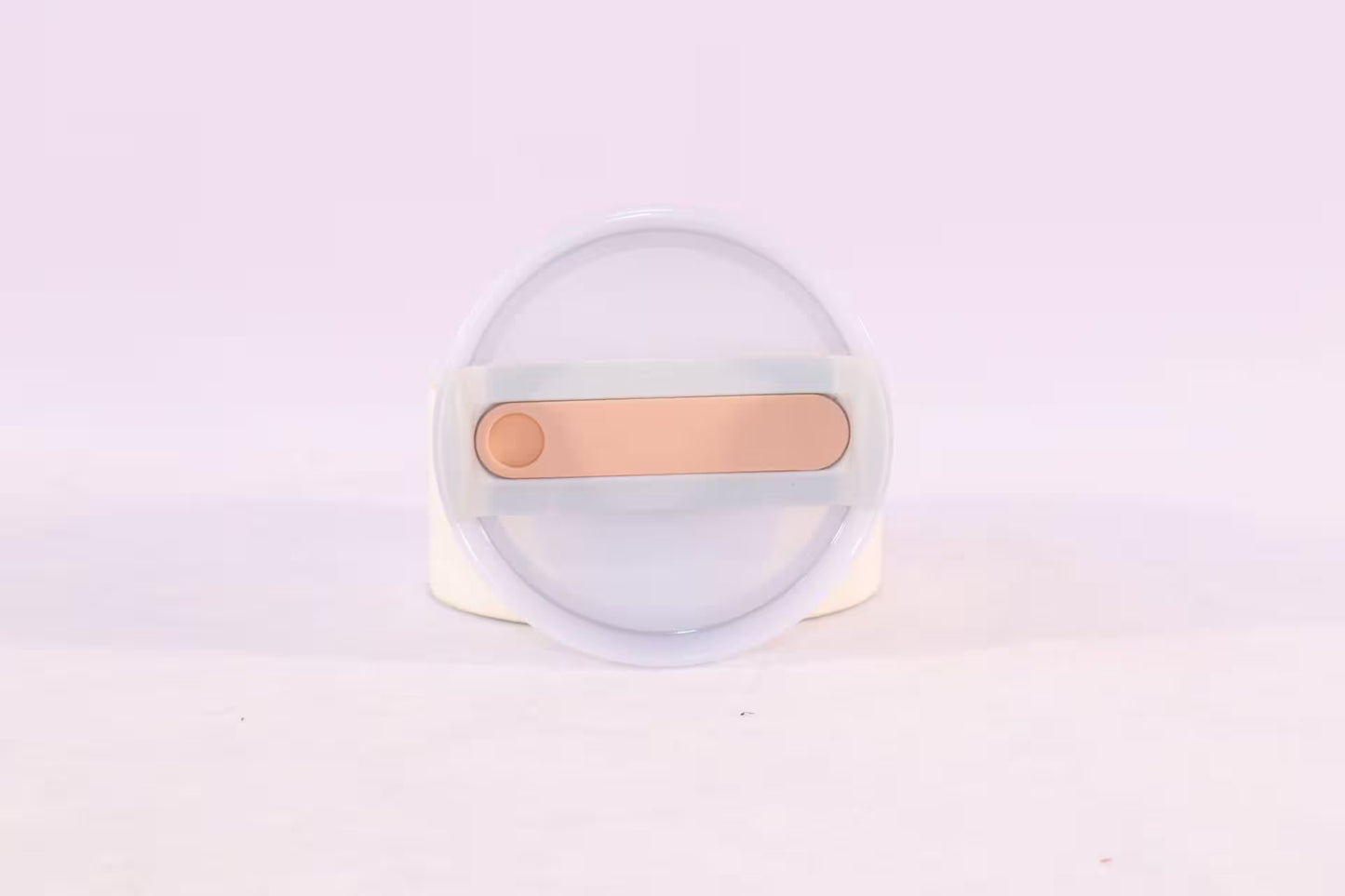 Round white object with a gold bar on a light purple background