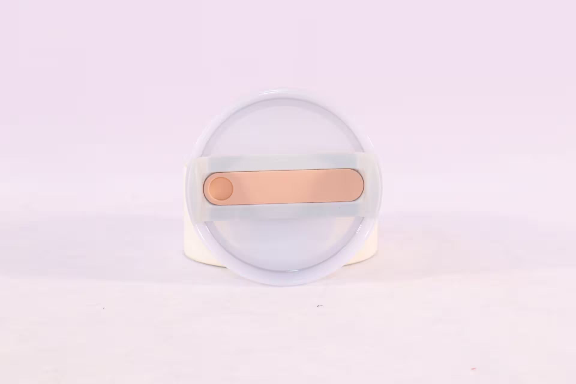 Round white object with a gold bar on a light purple background