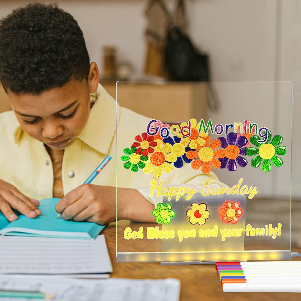 Child writing in a notebook with a decorative sign reading 'Good Morning Happy Sunday God Bless you and your family!' in the foreground.
