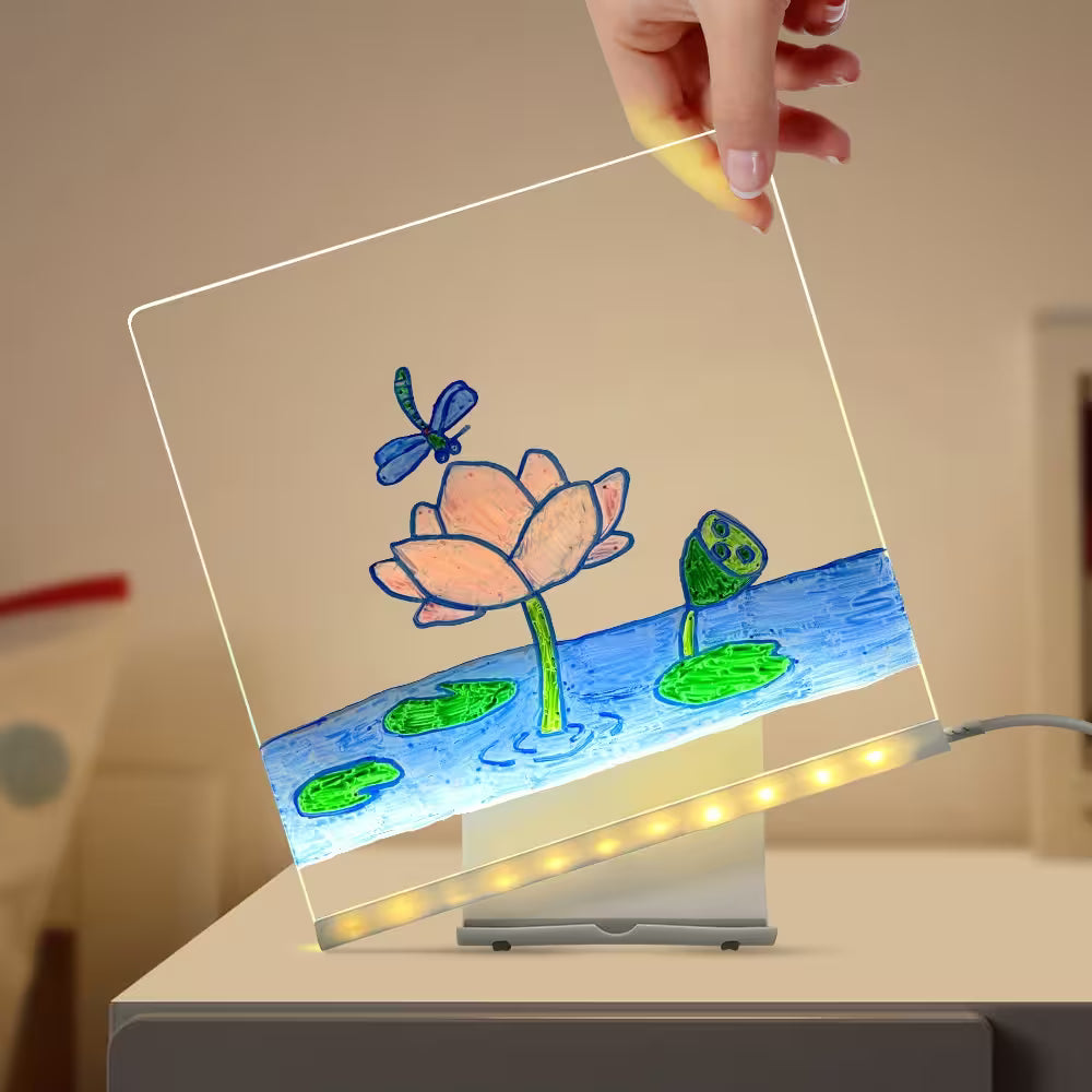 Transparent LED panel with a colorful drawing of a pond, frog, and dragonfly, held by a hand.