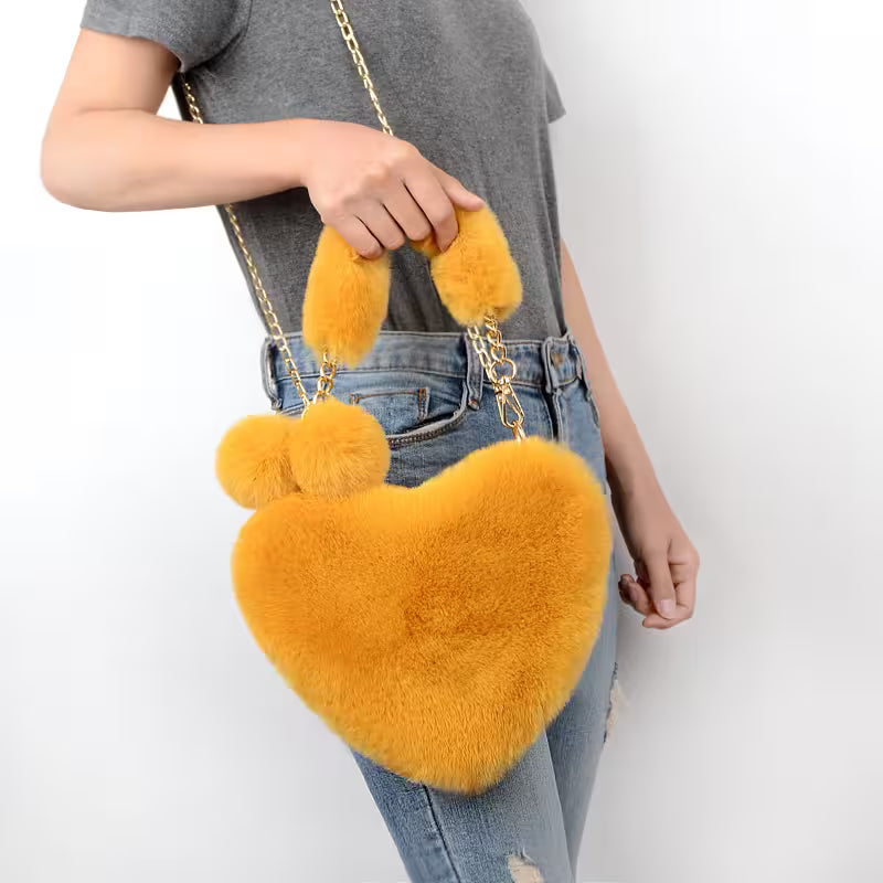 Person holding a yellow heart-shaped fluffy bag with chain strap on a white background