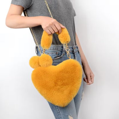 Person holding a yellow heart-shaped fluffy bag with chain strap on a white background