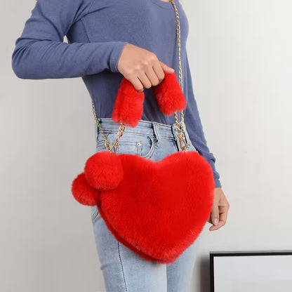 Person holding a red heart-shaped bag with pom-pom details against a plain background
