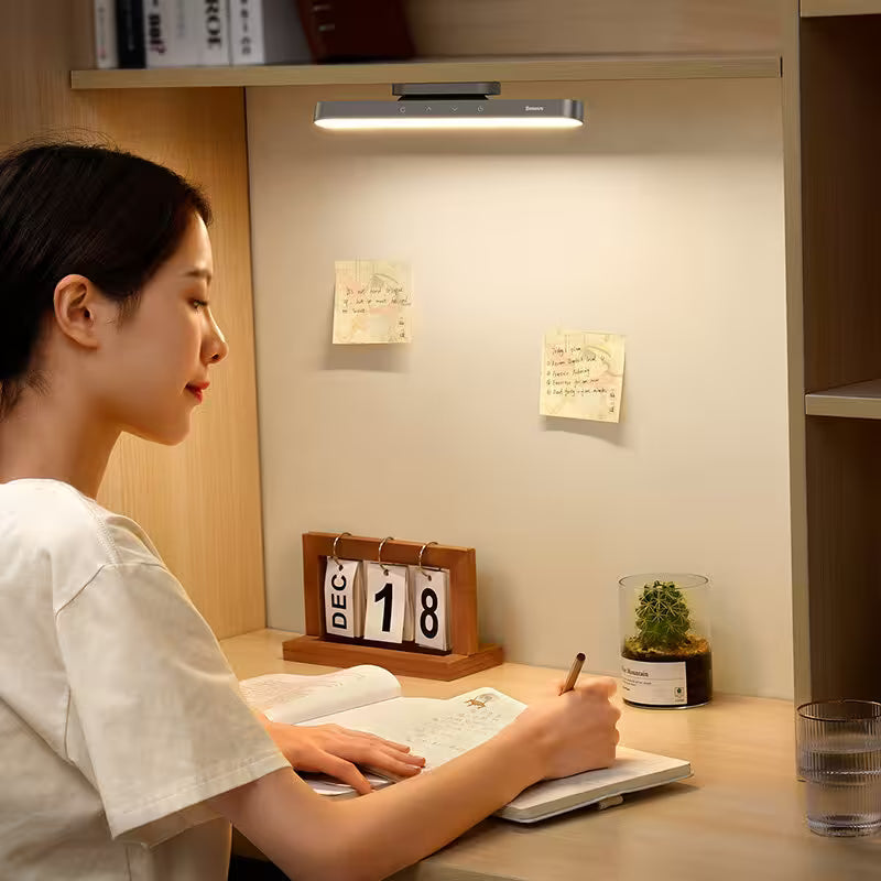Person studying at a desk with a light fixture above, near a calendar and plant.