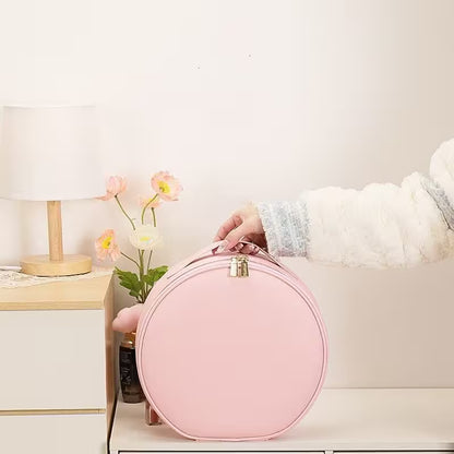 Person holding a pink round bag in a home setting with a lamp and flowers in the background.
