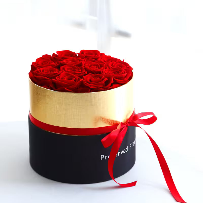 Round black box with gold top and red ribbon containing red roses on a white background