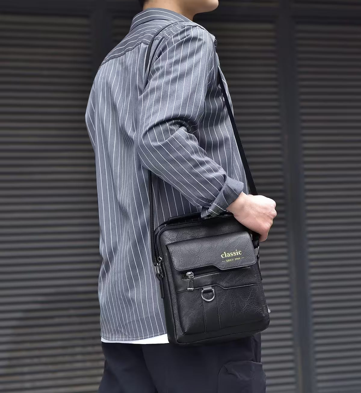 Person holding a black leather bag with 'classic' branding against a gray background