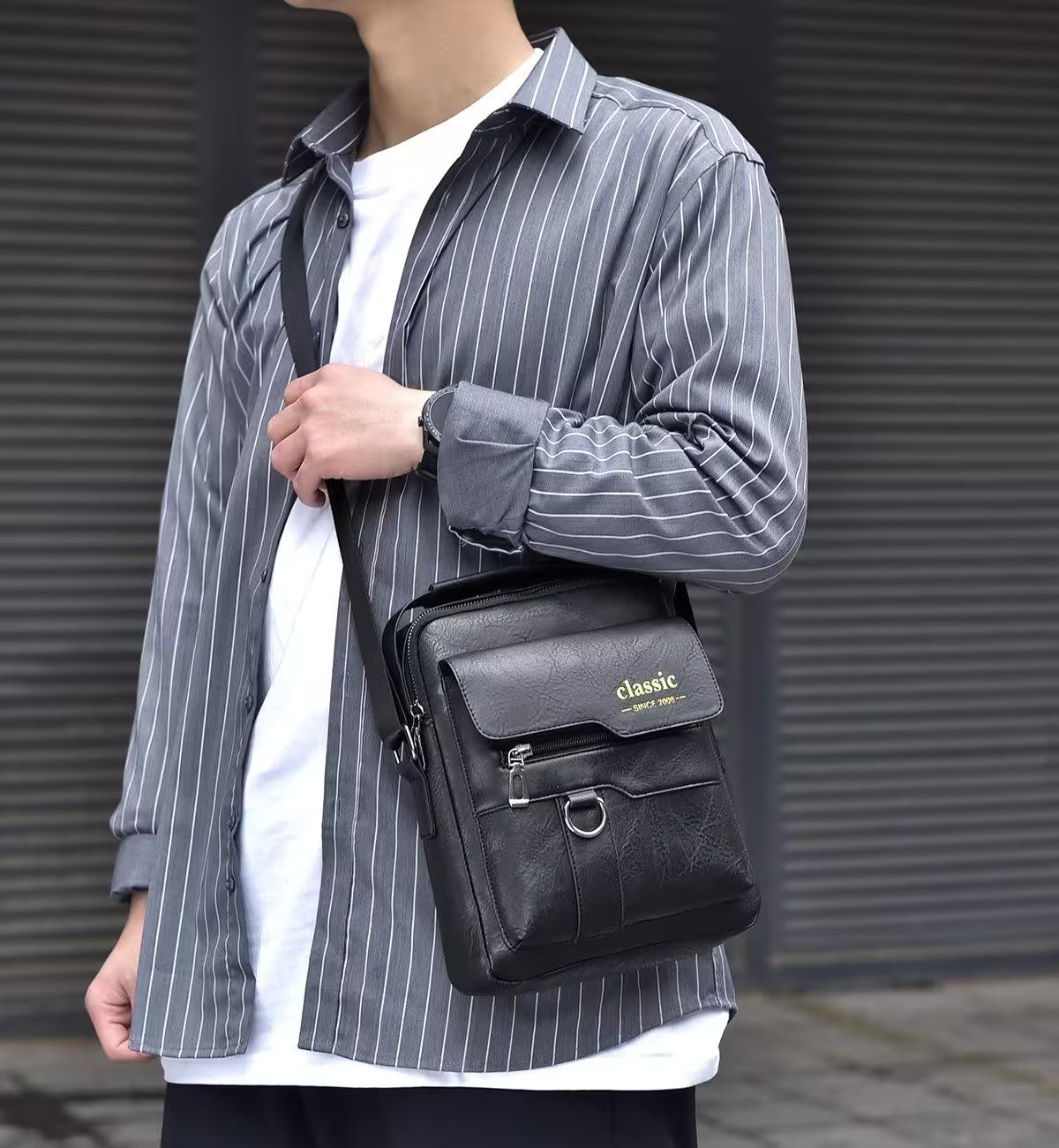 Person wearing a gray striped shirt holding a black leather bag with 'classic' branding.