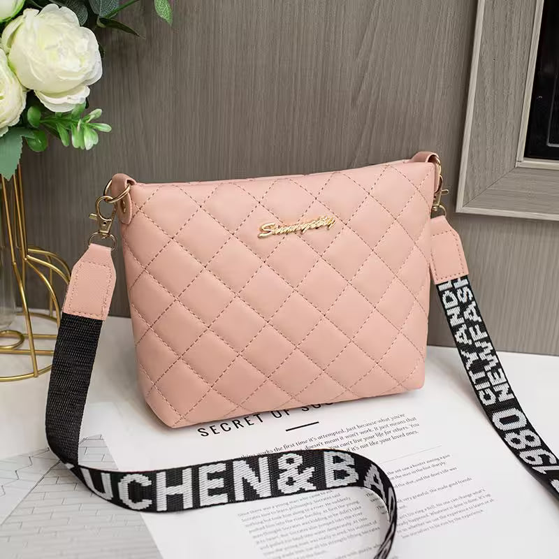 Pink quilted handbag with a black and white strap on a surface with flowers and a book in the background.