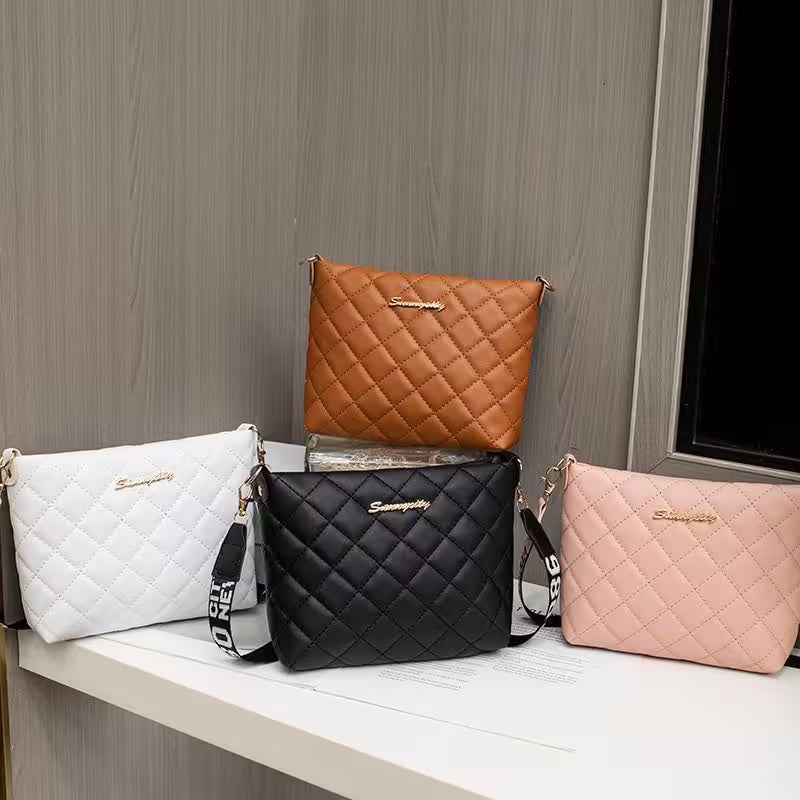 Four quilted handbags in white, brown, black, and pink on a wooden surface with a gray wall background.
