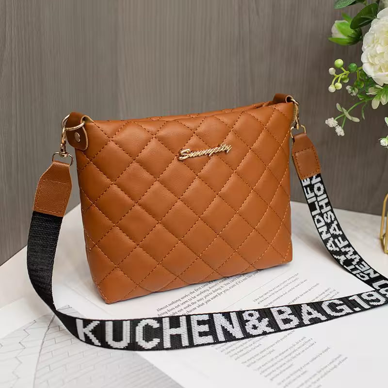 Brown quilted handbag with a black strap on a wooden surface