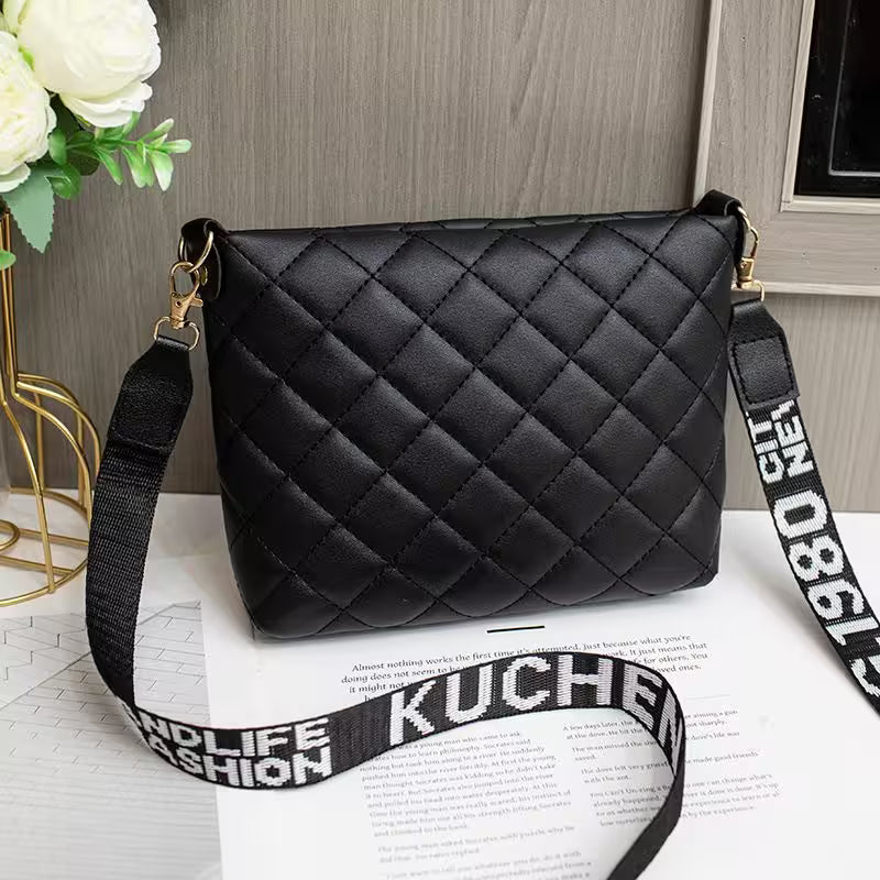Black quilted handbag with a branded strap on a surface with flowers in the background