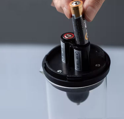 Hand inserting batteries into a device on a reflective surface with a dark background