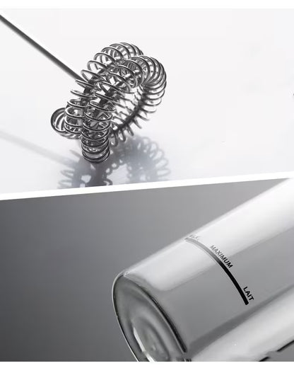 Metallic whisk on a reflective surface with a blurred kitchen appliance in the foreground
