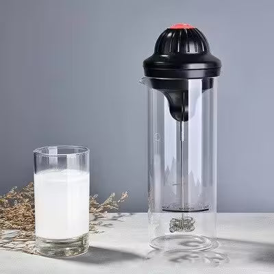 Clear shaker with black top next to a glass of milk on a gray background
