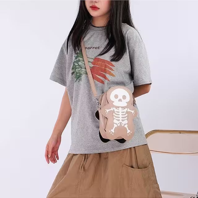 Person wearing a gray t-shirt with a graphic design, holding a small bag with a skeleton design.