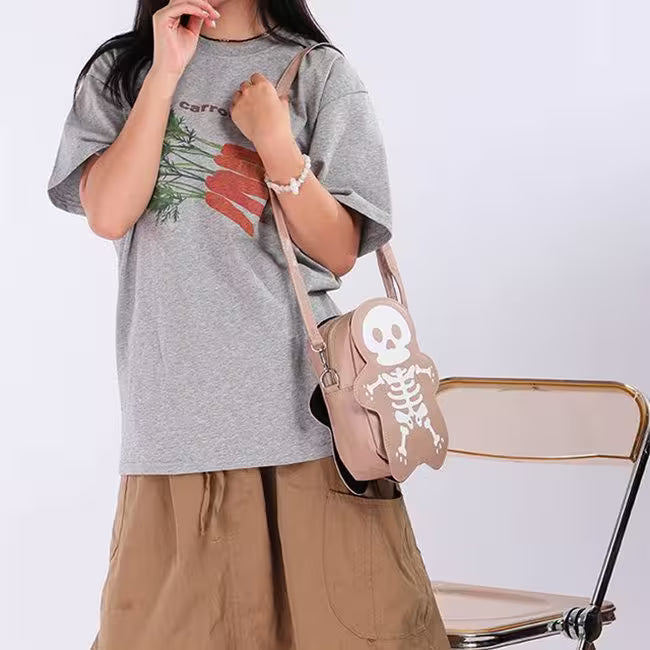 Person wearing a gray t-shirt with a carrot design and holding a beige bag with a skeleton design.