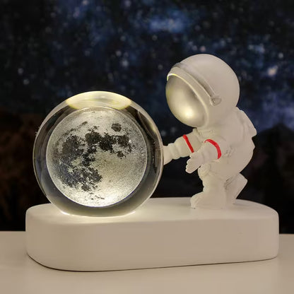 Decorative piece with a moon globe and an astronaut figure against a starry night sky background.