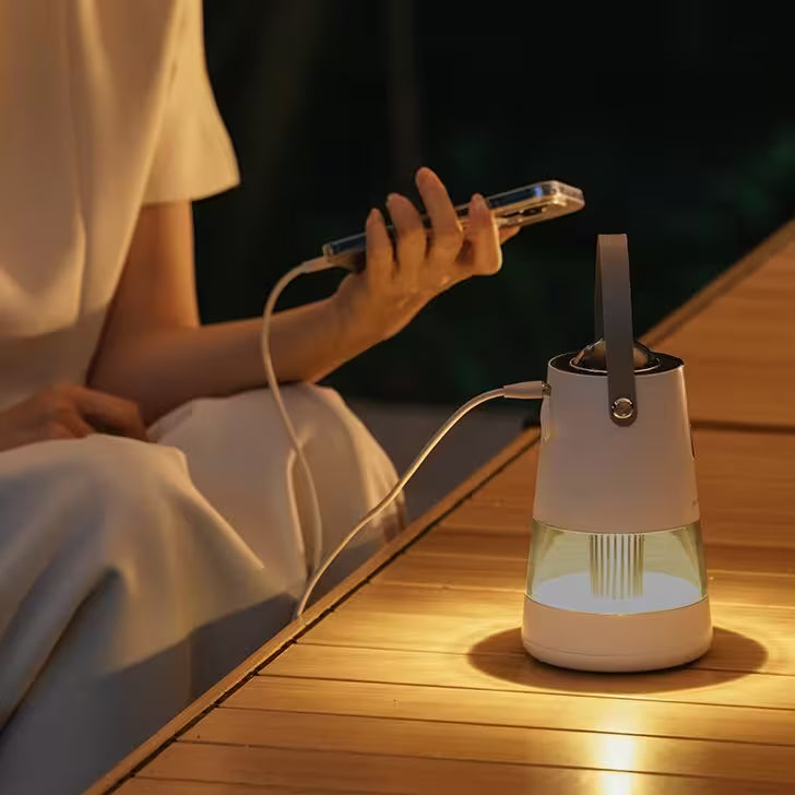 Person using a smartphone next to a portable lamp on a wooden surface at night.
