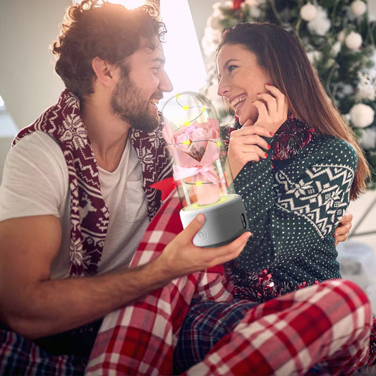 Man and woman sitting together holding a glowing snow globe with a Christmas tree in the background
