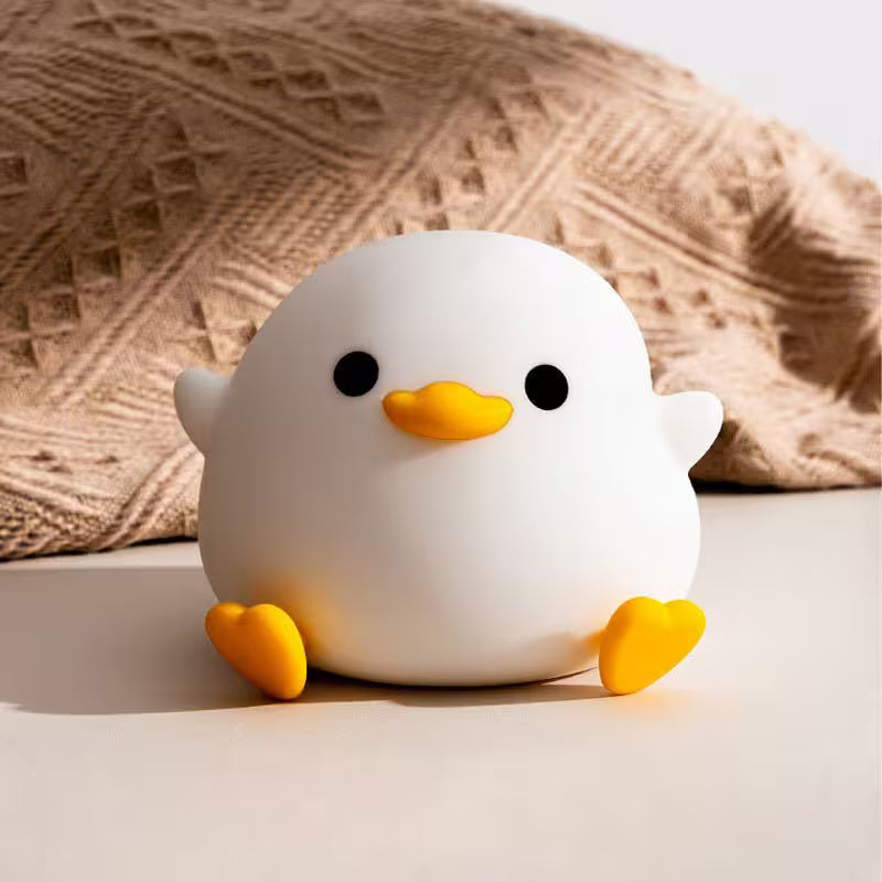 White duck-shaped toy with yellow feet and beak on a light surface with a textured beige background