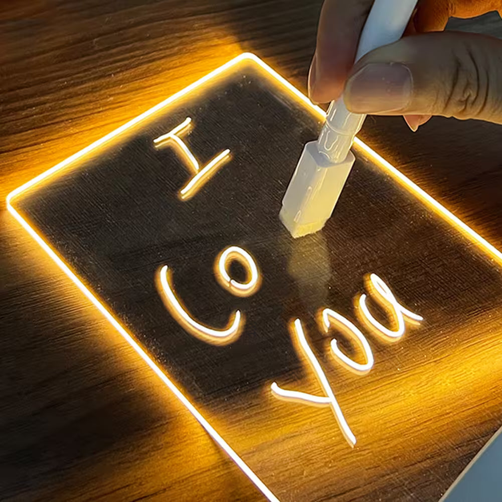 Hand writing 'I love you' on a wooden board with a pen, illuminated by warm light.