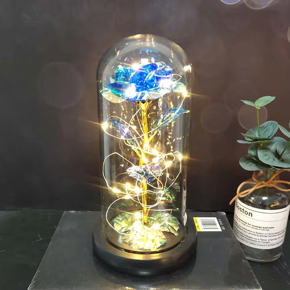 Decorative glass dome with a blue rose and fairy lights on a dark surface.