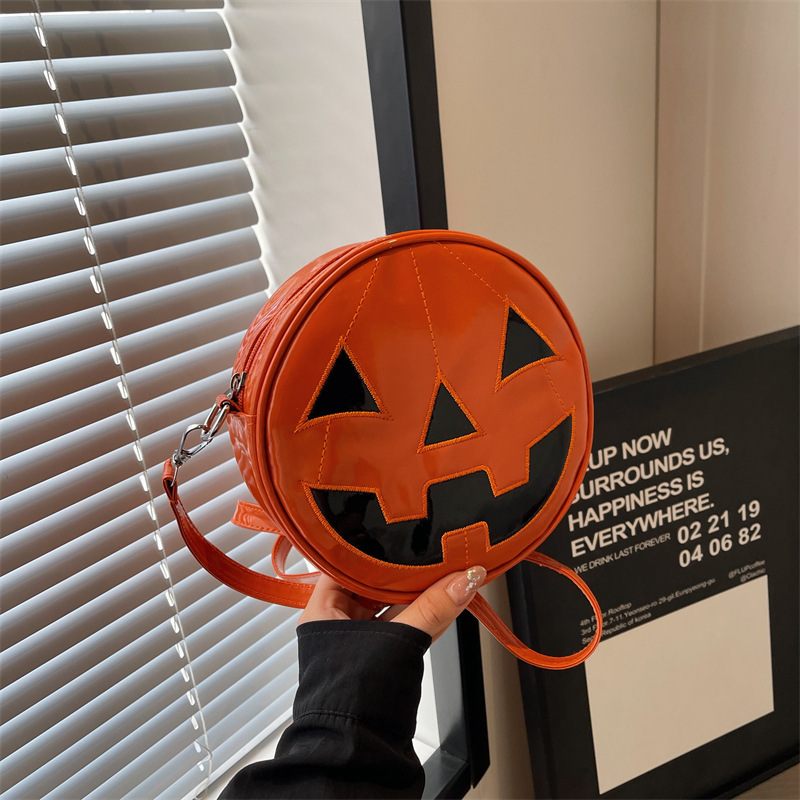Orange pumpkin-shaped bag with a face design held by a hand in front of a window.