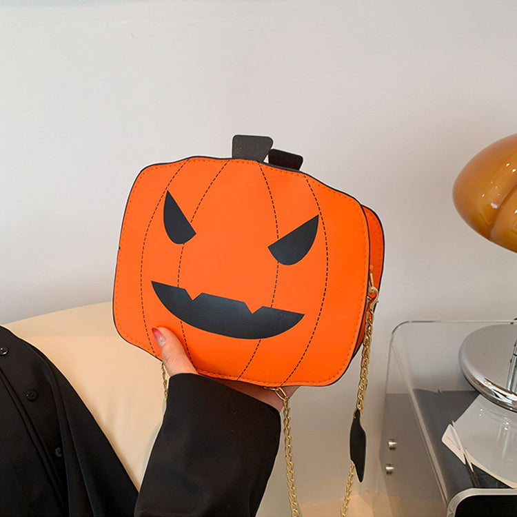 Pumpkin-shaped handbag with a face design held by a person against a neutral background