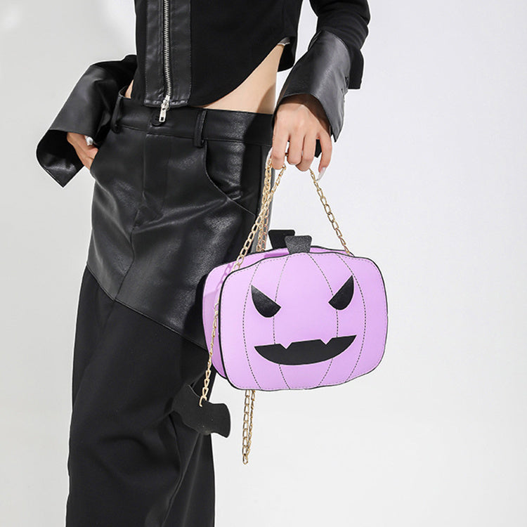 Person holding a purple pumpkin-shaped handbag with a chain strap on a plain background