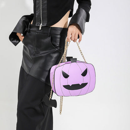 Person holding a purple pumpkin-shaped handbag with a chain strap on a plain background
