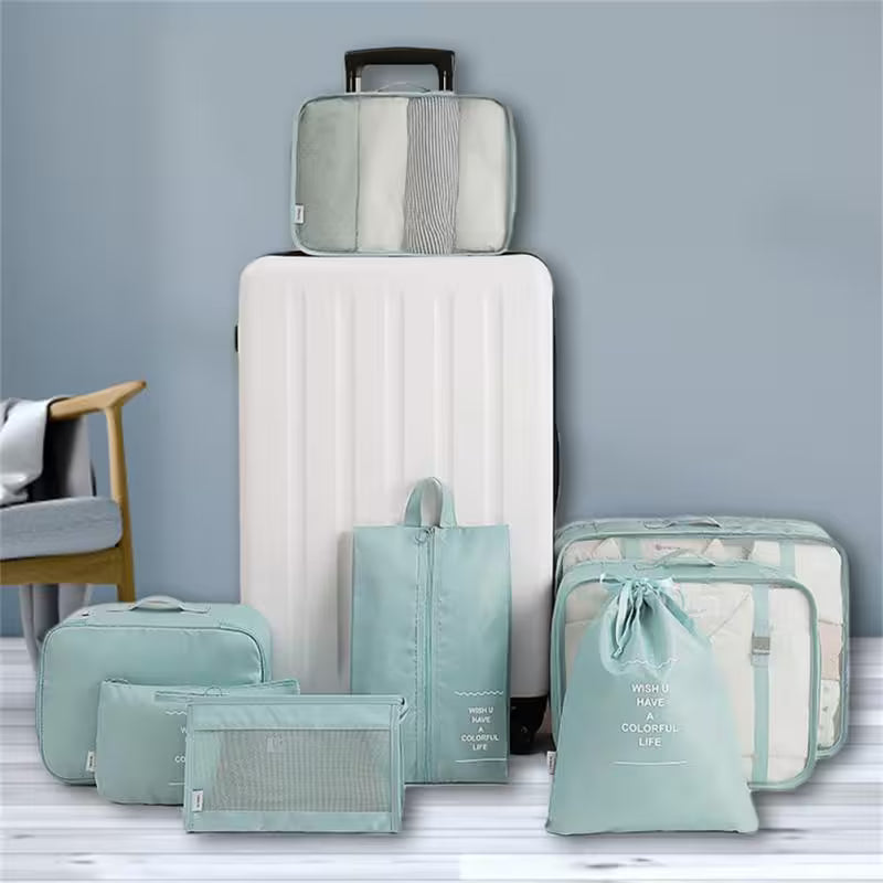 Set of green packing cubes and a white suitcase on a light gray surface with a neutral background.