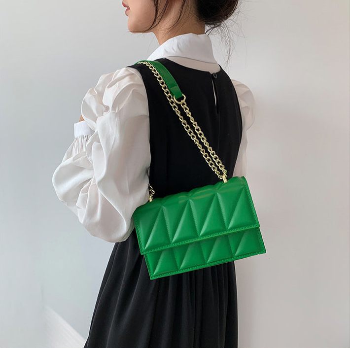 Person wearing a green quilted handbag with a gold chain strap on a plain background