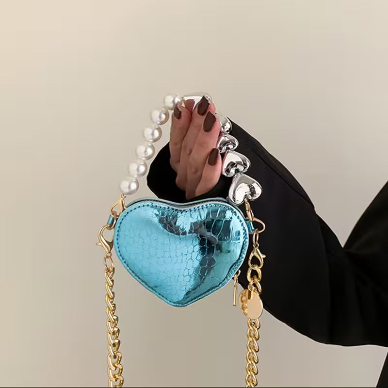 Heart-shaped blue handbag with pearl handle held by a person against a beige background