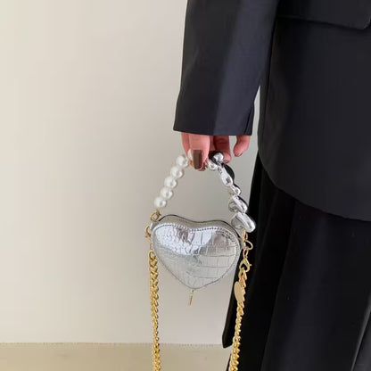 Heart-shaped handbag with pearl handle held by a person wearing a black coat.