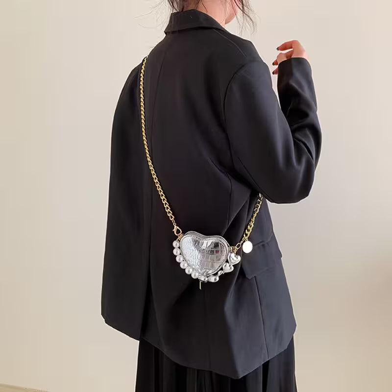 Person wearing a black coat with a decorative heart-shaped bag on a plain background