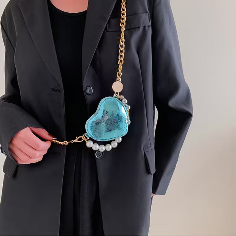 Person holding a blue heart-shaped bag with a gold chain and pearl details.