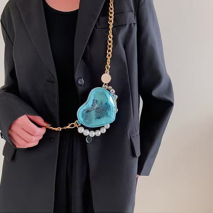 Person holding a blue heart-shaped bag with a gold chain and pearl details.