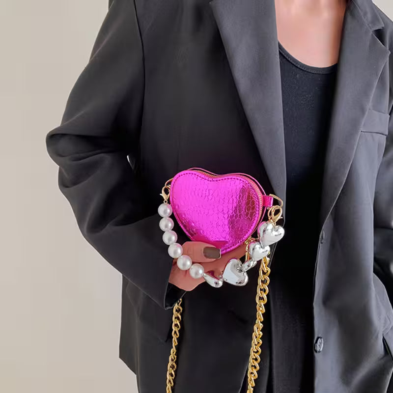 Person holding a pink heart-shaped handbag with pearl and chain details.