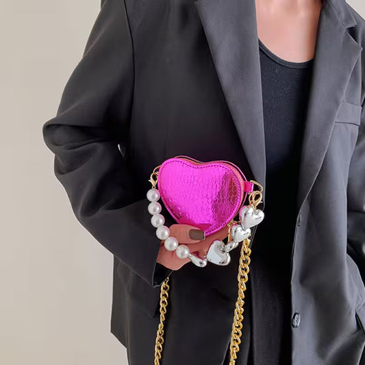 Person holding a pink heart-shaped handbag with pearl and chain details.