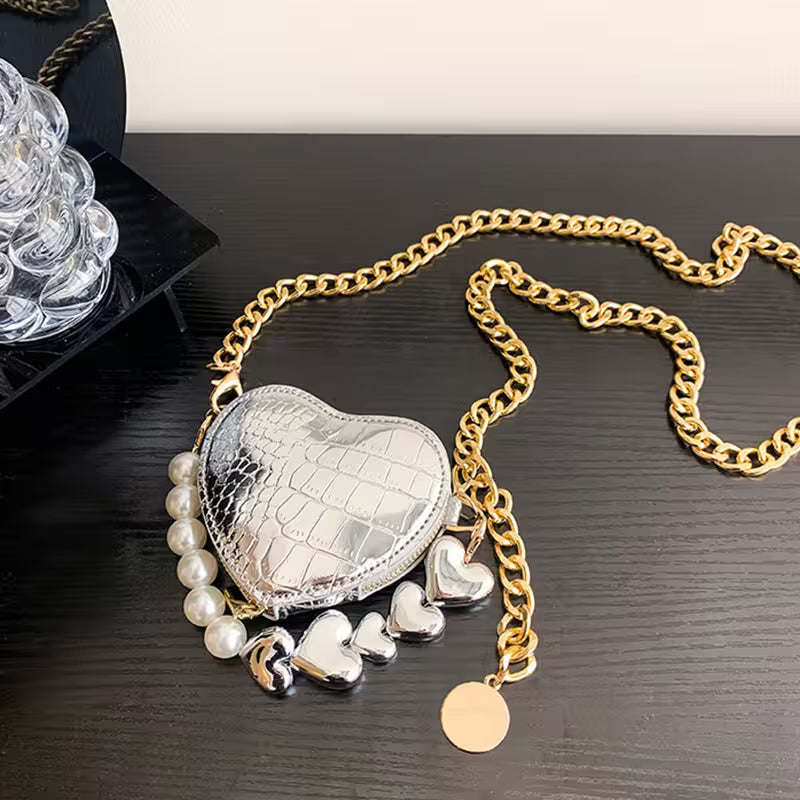 Heart-shaped silver purse with gold chain and charms on a dark surface