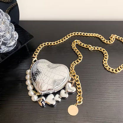 Heart-shaped silver purse with gold chain and charms on a dark surface